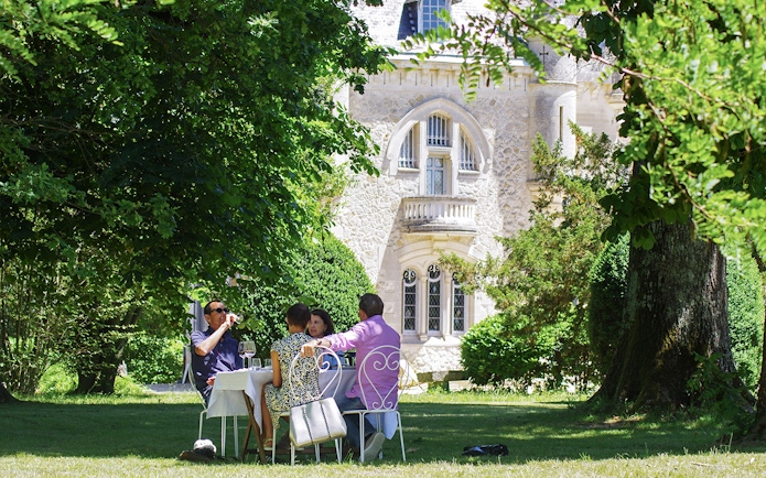 Group enjoying wine at a table in a garden near a historic building in Saint-Emilion.