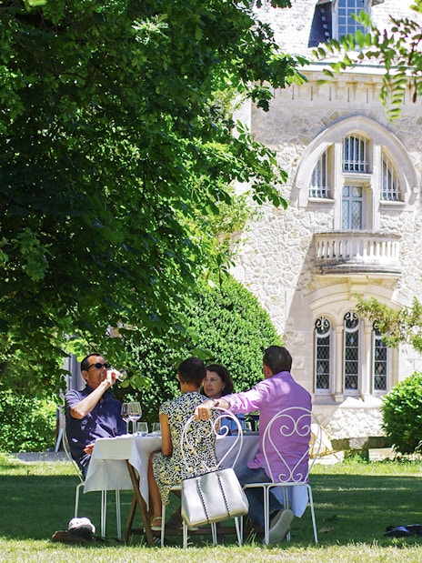 Group enjoying wine at a table in a garden near a historic building in Saint-Emilion.