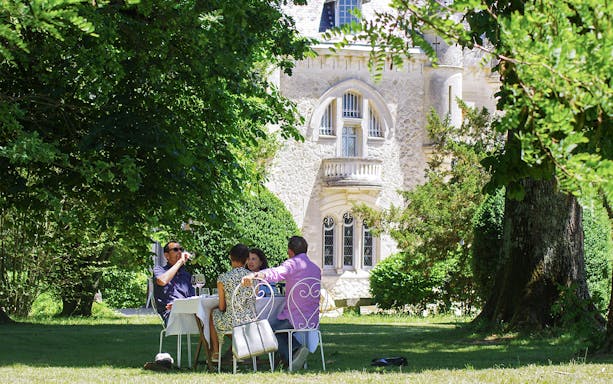 Group enjoying wine at a table in a garden near a historic building in Saint-Emilion.