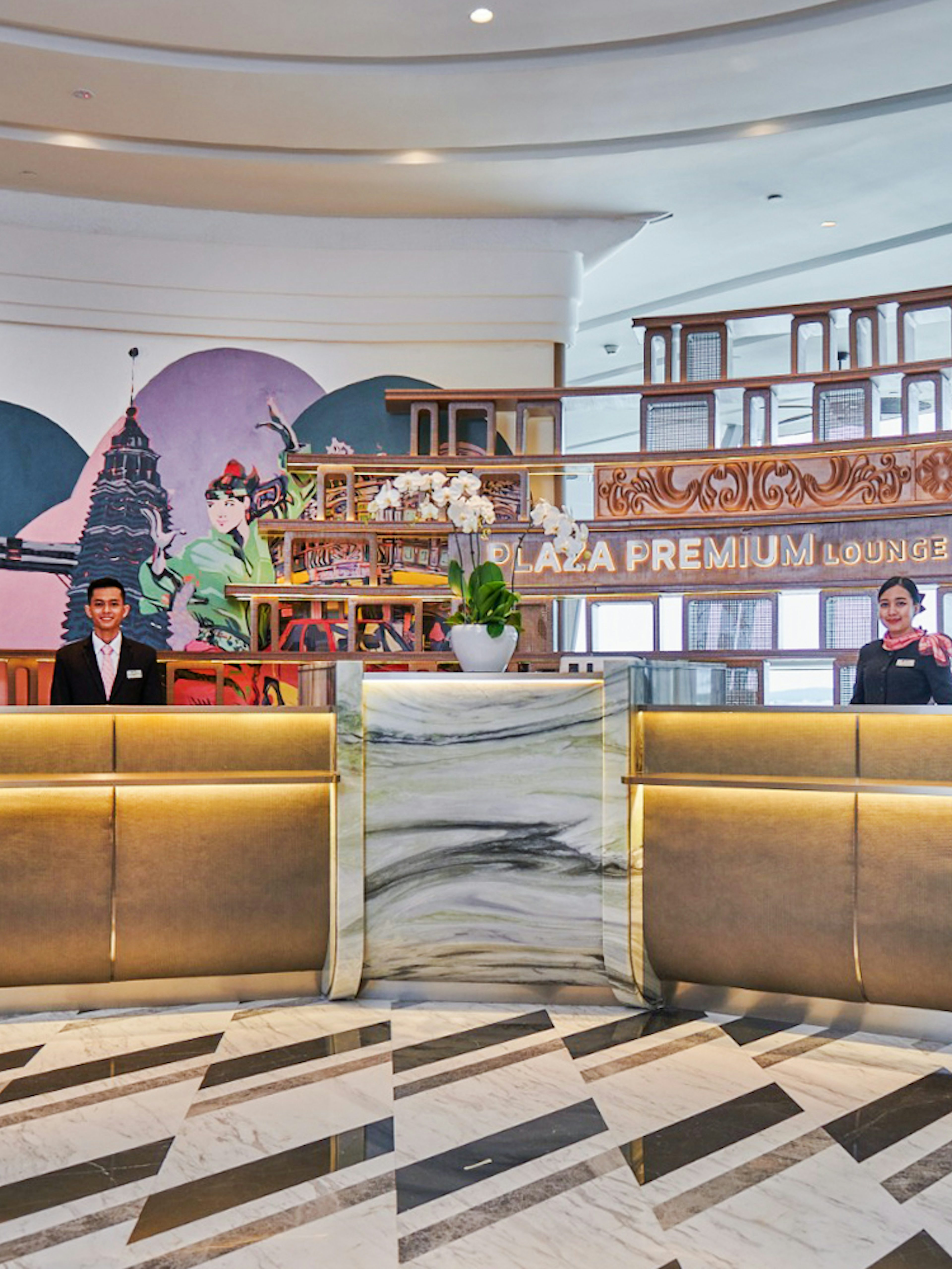 Reception area of Plaza Premium Lounge at KLIA Terminal 1 with staff and mural.