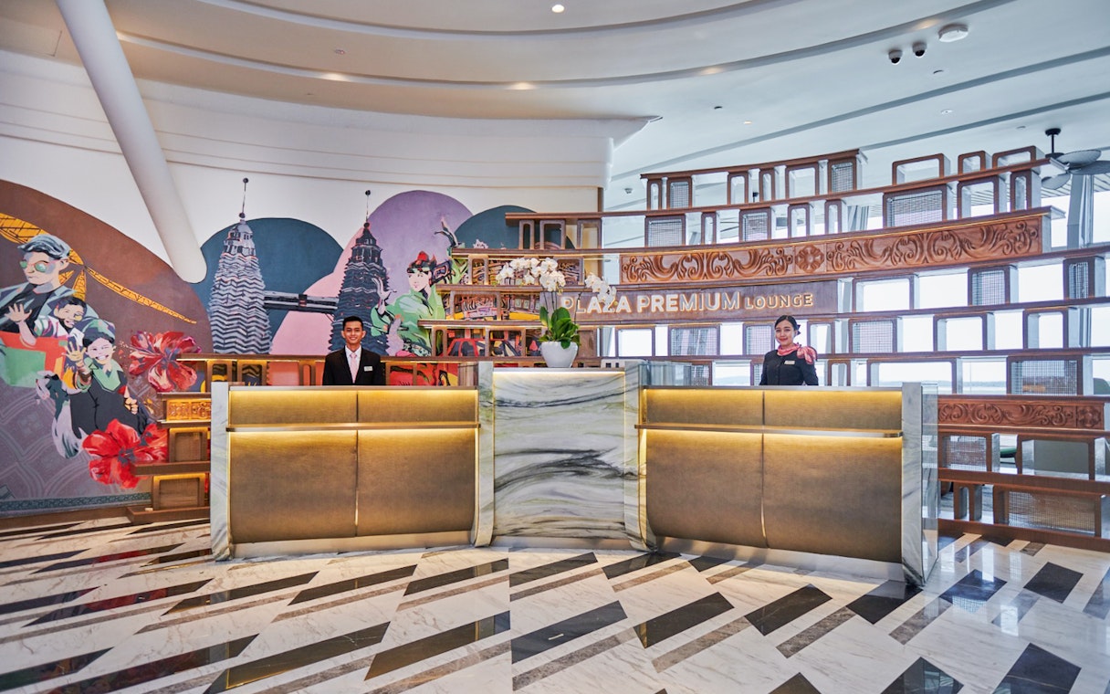Reception area of Plaza Premium Lounge at KLIA Terminal 1 with staff and mural.