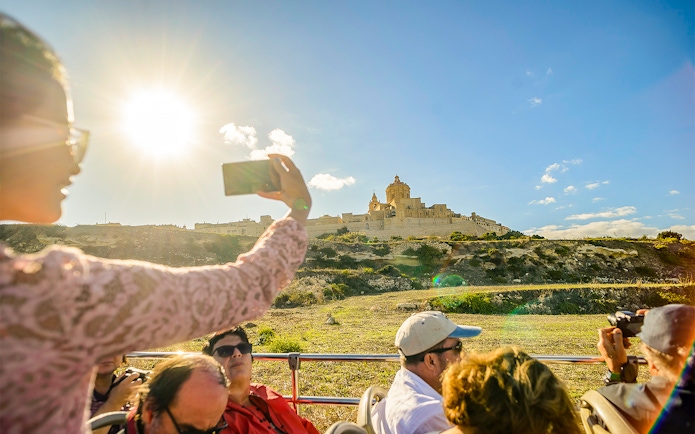 Tourists on an open-top bus viewing Mdina, Malta during a hop-on-hop-off tour.
