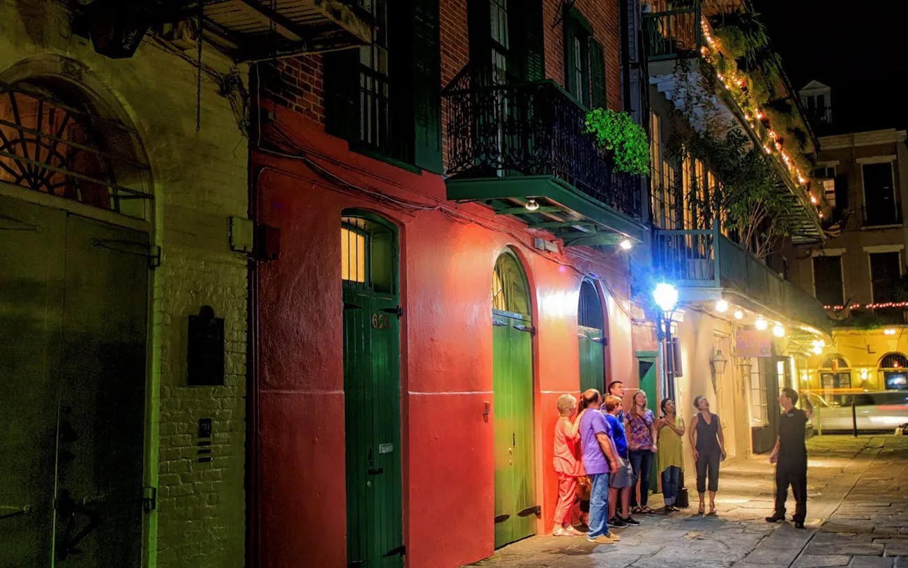 Group on New Orleans ghost tour at night, standing by historic French Quarter building.