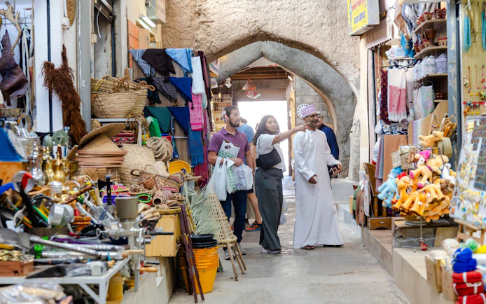 Visitors exploring shops in Nizwa Souq, Oman, with traditional crafts and souvenirs displayed.