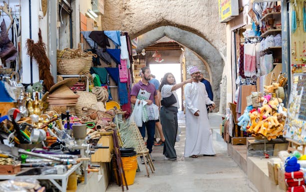Visitors exploring shops in Nizwa Souq, Oman, with traditional crafts and souvenirs displayed.