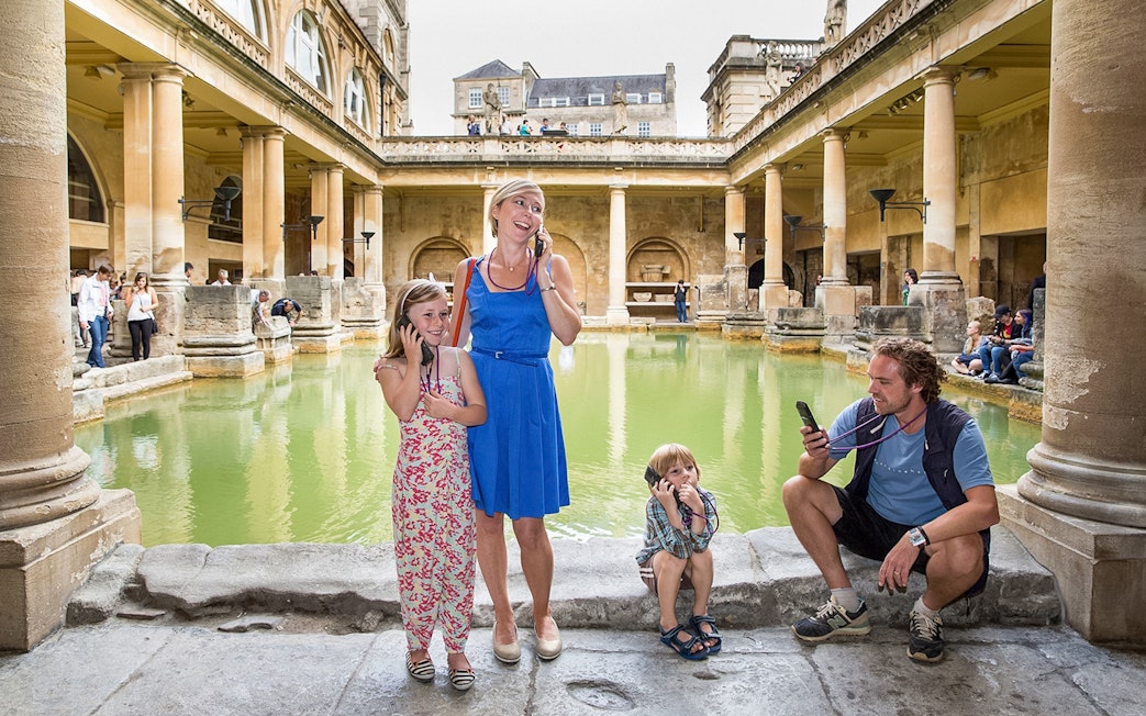 Family enjoying audio tour at Roman Baths, UK.