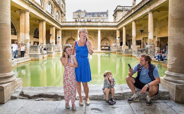 Family enjoying audio tour at Roman Baths, UK.