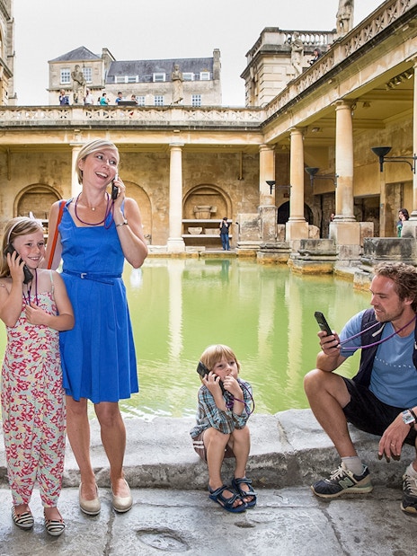Family enjoying audio tour at Roman Baths, UK.