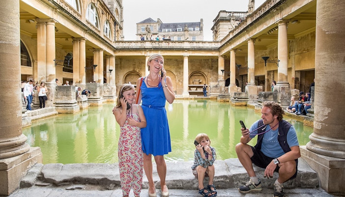 Family enjoying audio tour at Roman Baths, UK.
