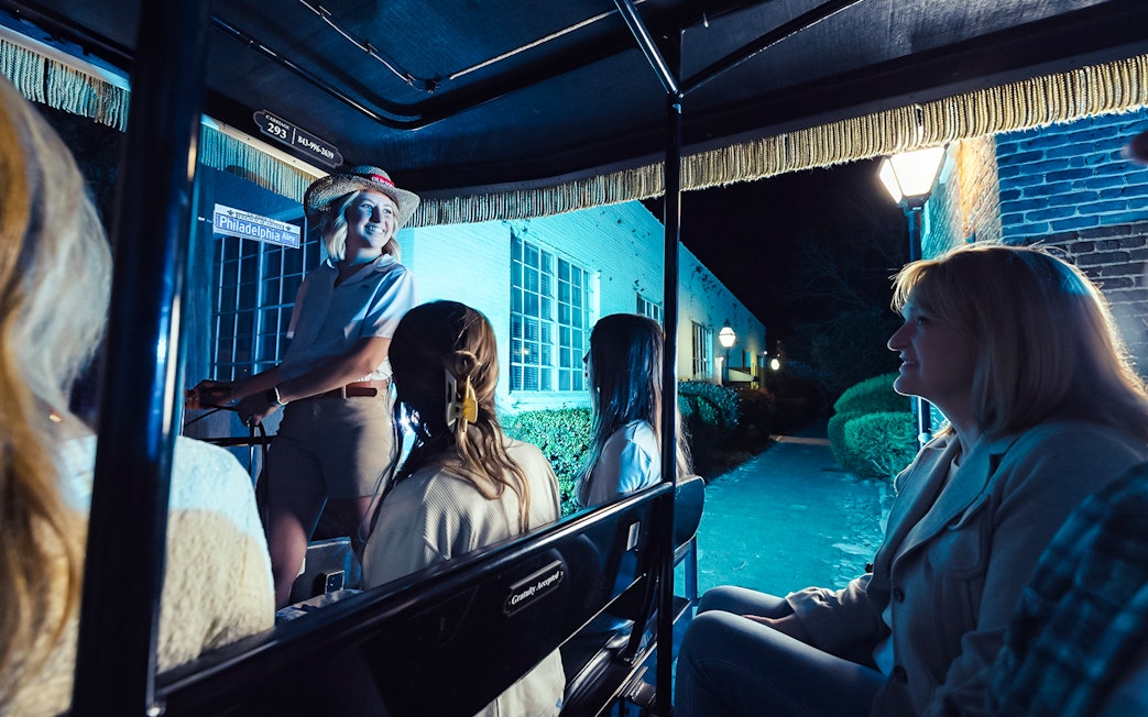 Carriage tour guide leading a group through Charleston's historic streets at night.