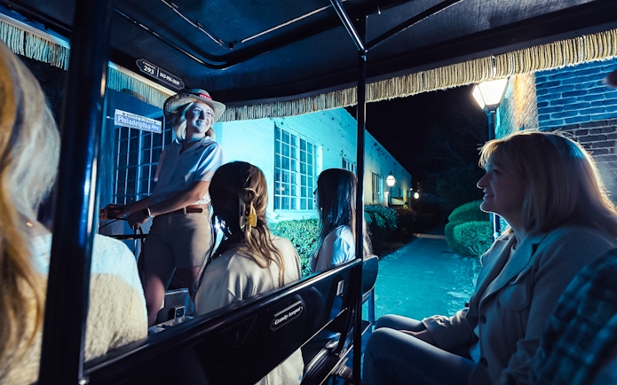 Carriage tour guide leading a group through Charleston's historic streets at night.