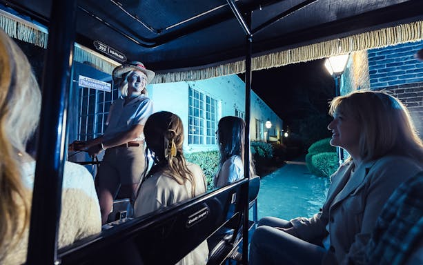 Carriage tour guide leading a group through Charleston's historic streets at night.