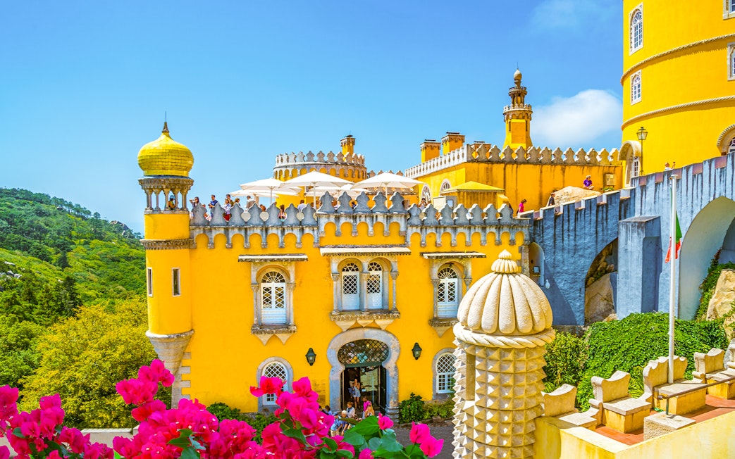 Pena Palace in Sintra, Portugal, with vibrant yellow facade and tourists exploring.