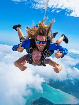 Skydivers freefalling over Airlie Beach with ocean and clouds below.