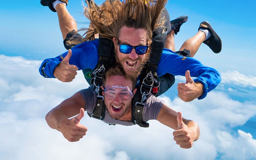 Skydivers freefalling over Airlie Beach with ocean and clouds below.