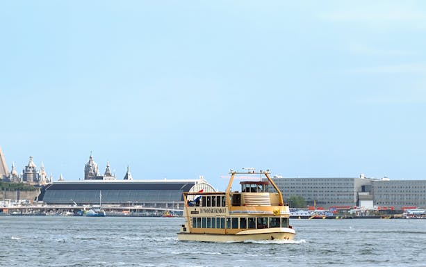 Tour boat on Amsterdam canal with cityscape in the background.
