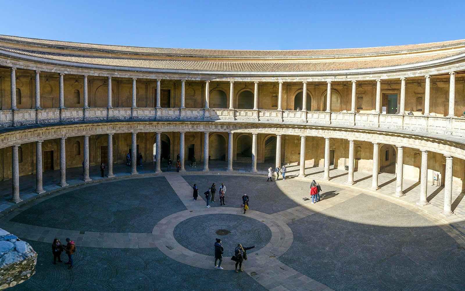 Circular courtyard of Carlos V Palace in Alhambra, Granada, with visitors exploring.