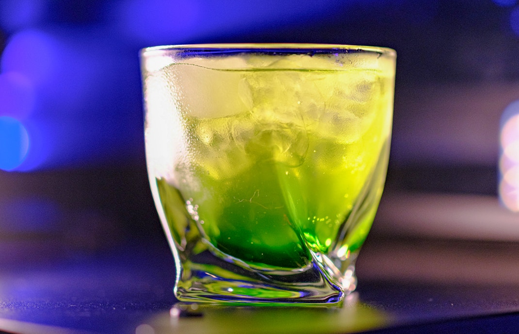 Green cocktail drink with a lime garnish on a bar counter in a vibrant setting.