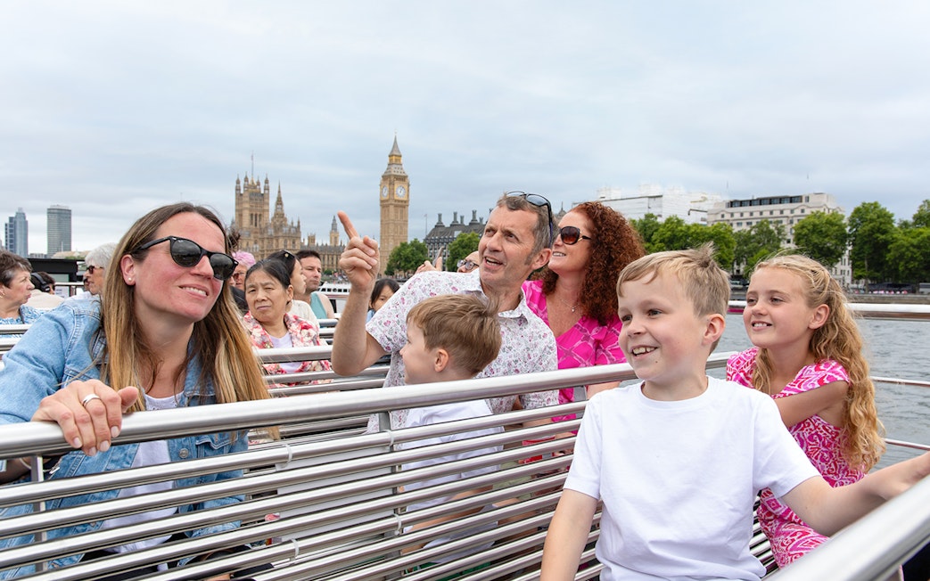 Family enjoying Thames river cruise with view of Big Ben, London.