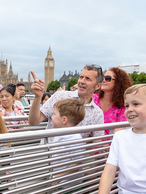 Family enjoying Thames river cruise with view of Big Ben, London.