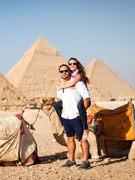 Couple with camels in front of the Pyramids at Giza Complex, Egypt.