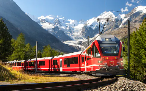 Red train traveling from Lucerne to Mount Titlis with snow-capped mountains in the background.