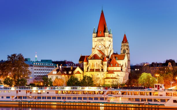 Cruise ship on Danube River with St. Francis of Assisi Church in Vienna at dusk.
