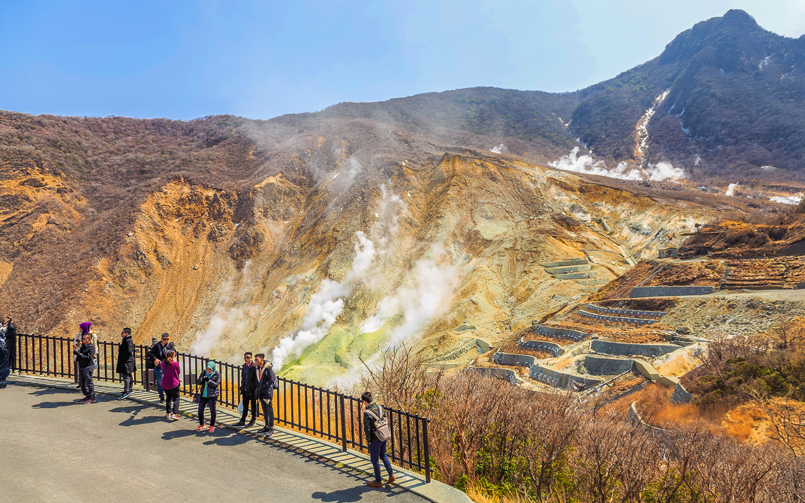 Visitors at Owakudani volcanic valley in Hakone, Japan, with steam rising from the ground.