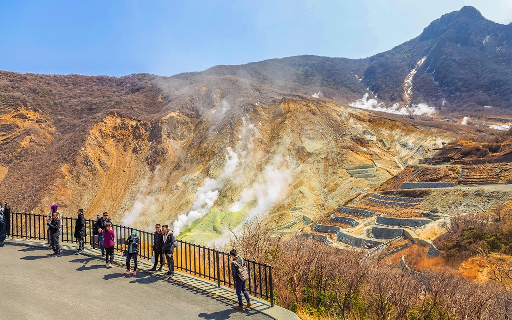 Visitors at Owakudani volcanic valley in Hakone, Japan, with steam rising from the ground.