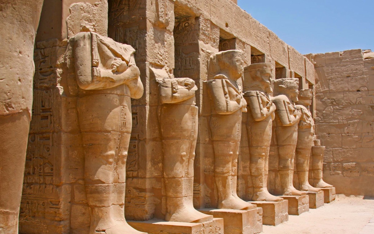Row of ancient statues at Karnak Temple, Egypt, under a clear sky.