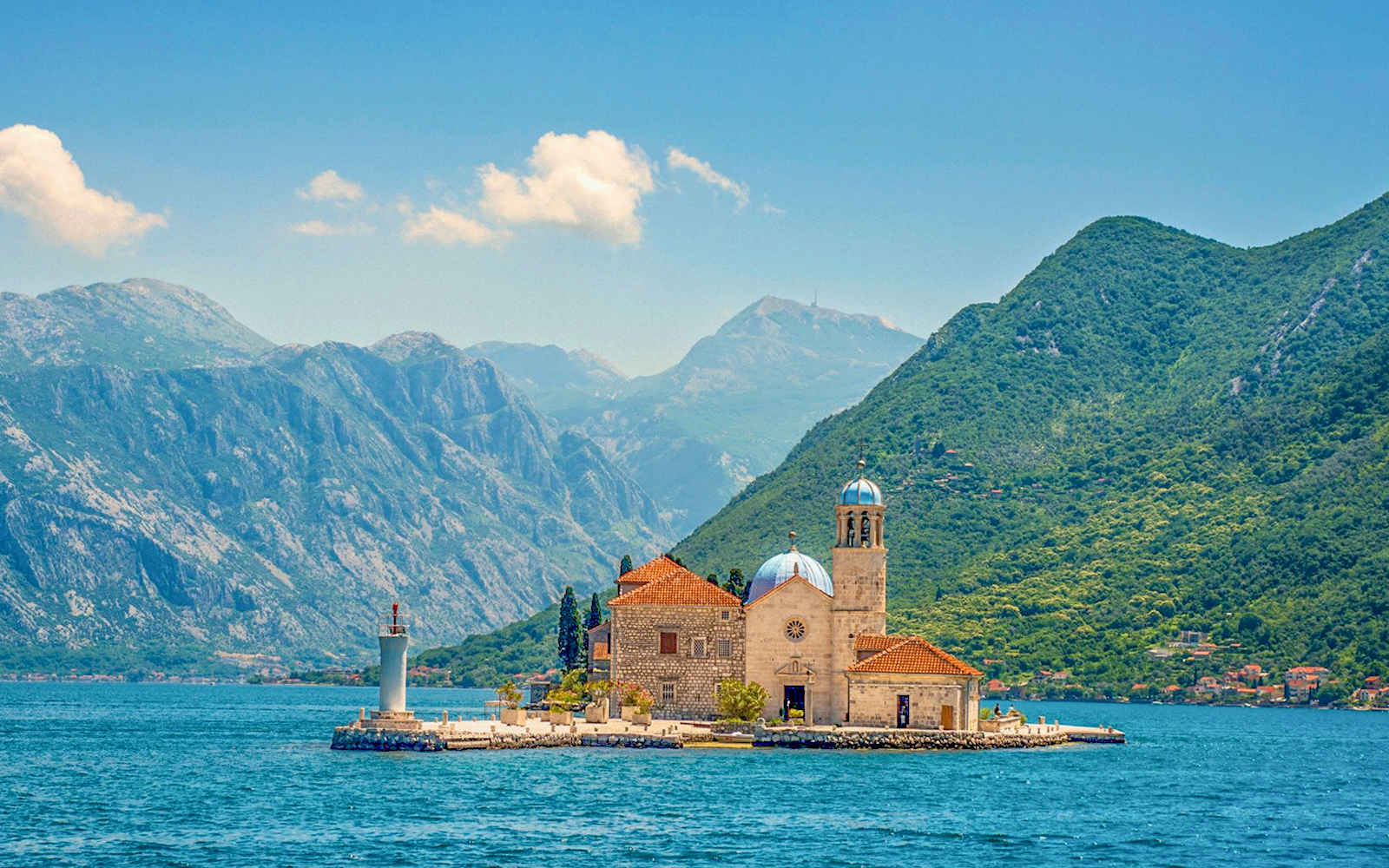 Our Lady of the Rocks island with church and lighthouse in Montenegro, surrounded by mountains.