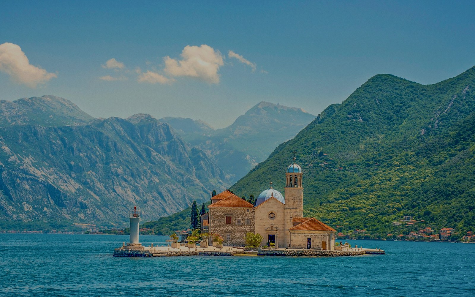 Our Lady of the Rocks island with church and lighthouse in Montenegro, surrounded by mountains.
