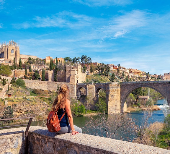 Woman sitting on a wall overlooking the Alcántara Bridge in Toledo, Spain.