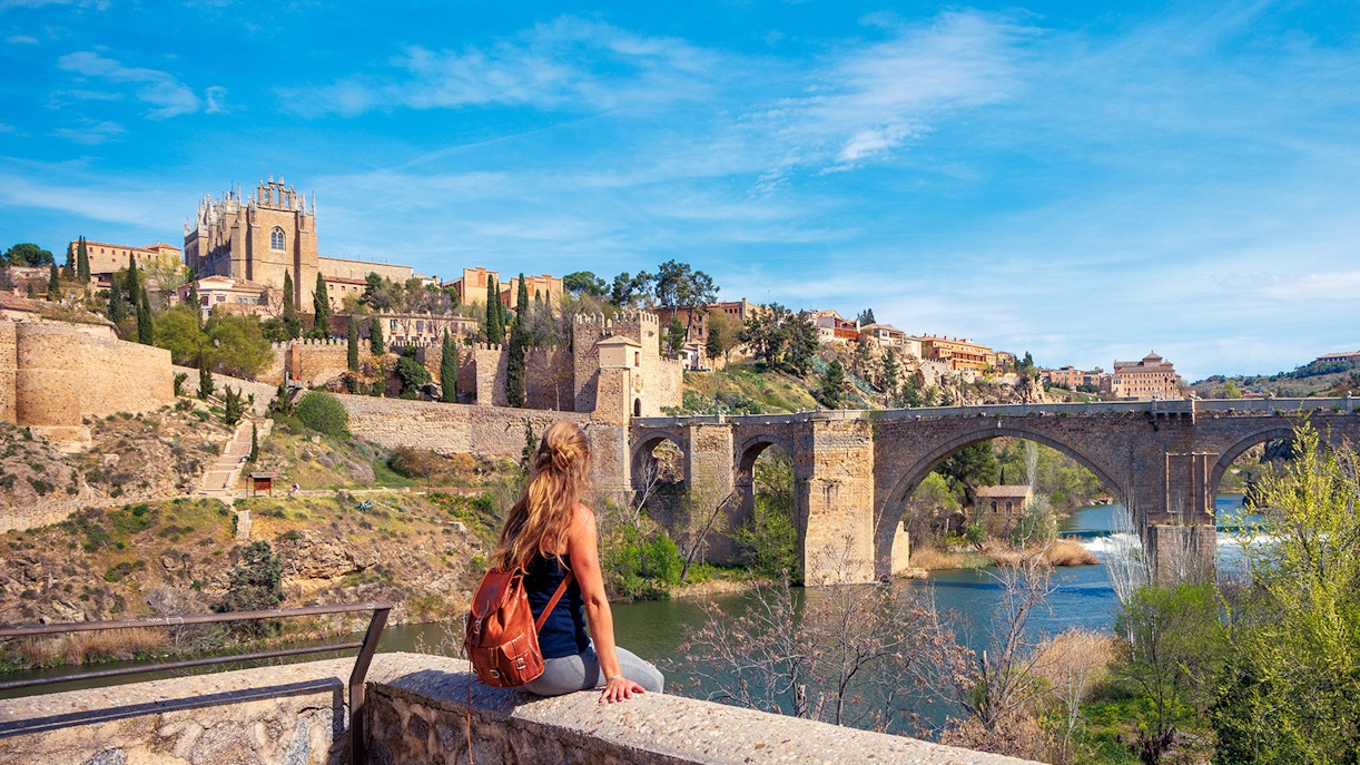Woman sitting on a wall overlooking the Alcántara Bridge in Toledo, Spain.
