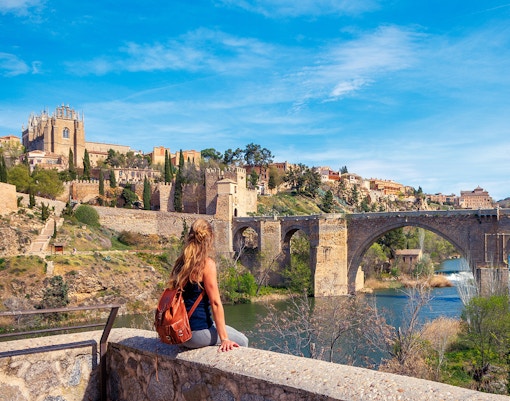 Woman sitting on a wall overlooking the Alcántara Bridge in Toledo, Spain.