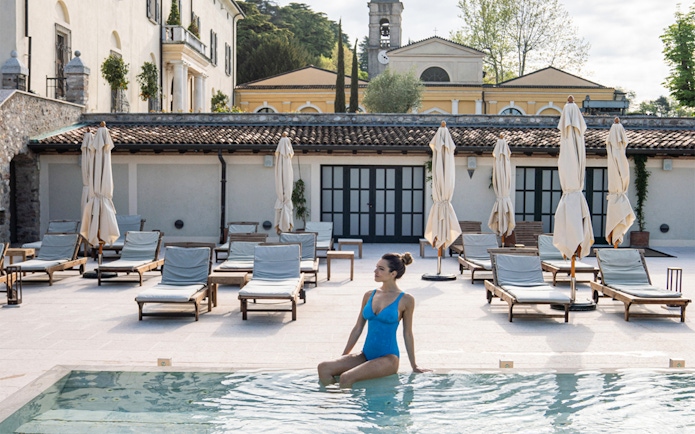 Person relaxing by the pool at QC Terme Garda, Italy, with loungers and umbrellas in the background.