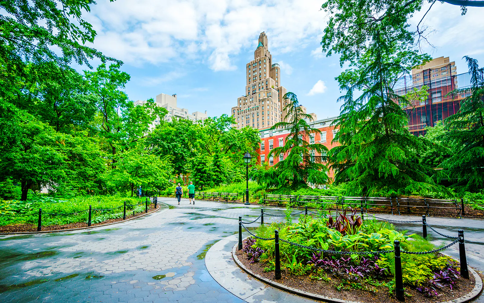 Pathway through Washington Square Park with lush greenery and historic buildings in Manhattan, NYC.