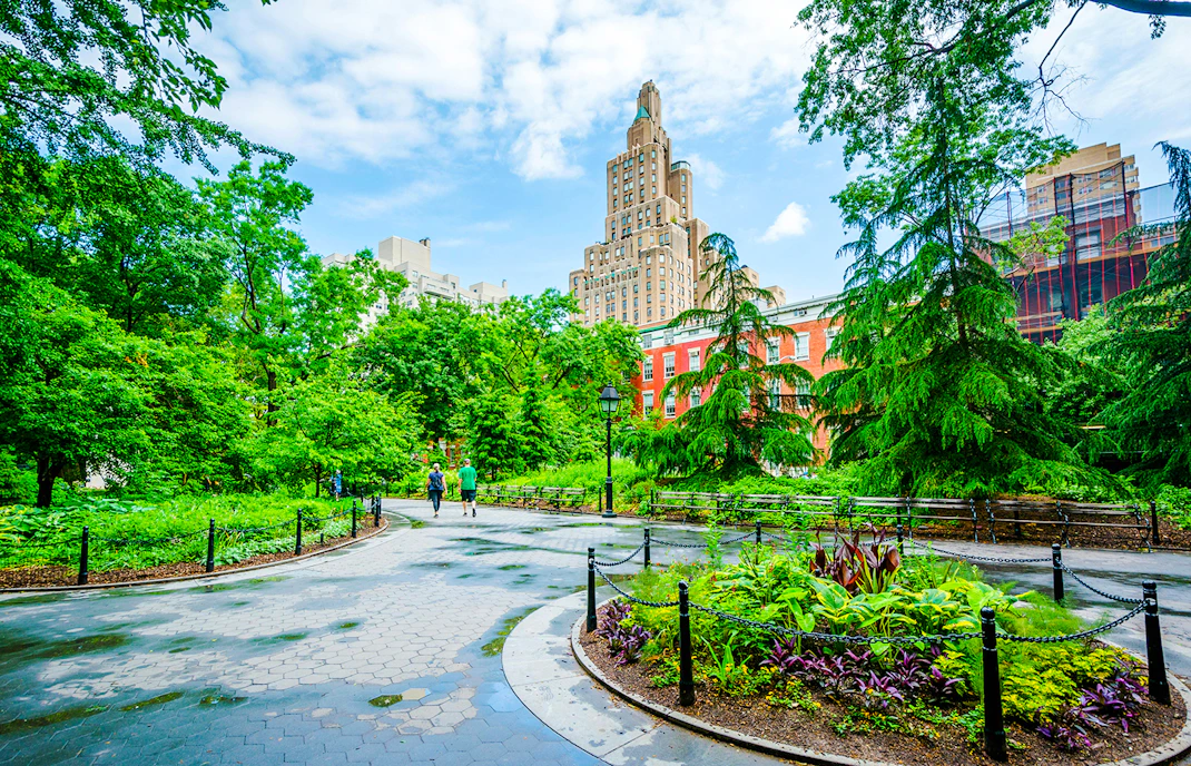 Pathway through Washington Square Park with lush greenery and historic buildings in Manhattan, NYC.