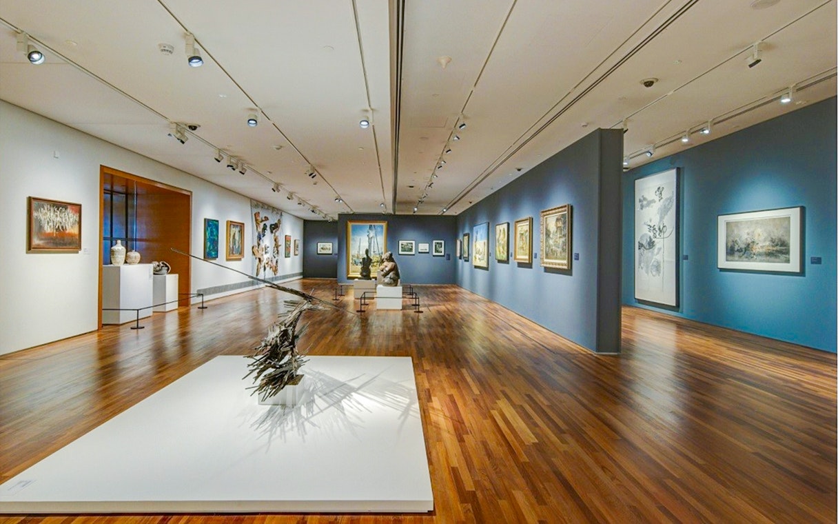 National Gallery Singapore interior with diverse art exhibits displayed on walls and sculptures on the floor.