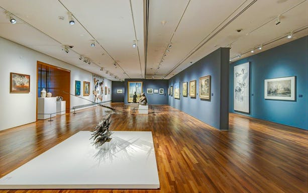 National Gallery Singapore interior with diverse art exhibits displayed on walls and sculptures on the floor.