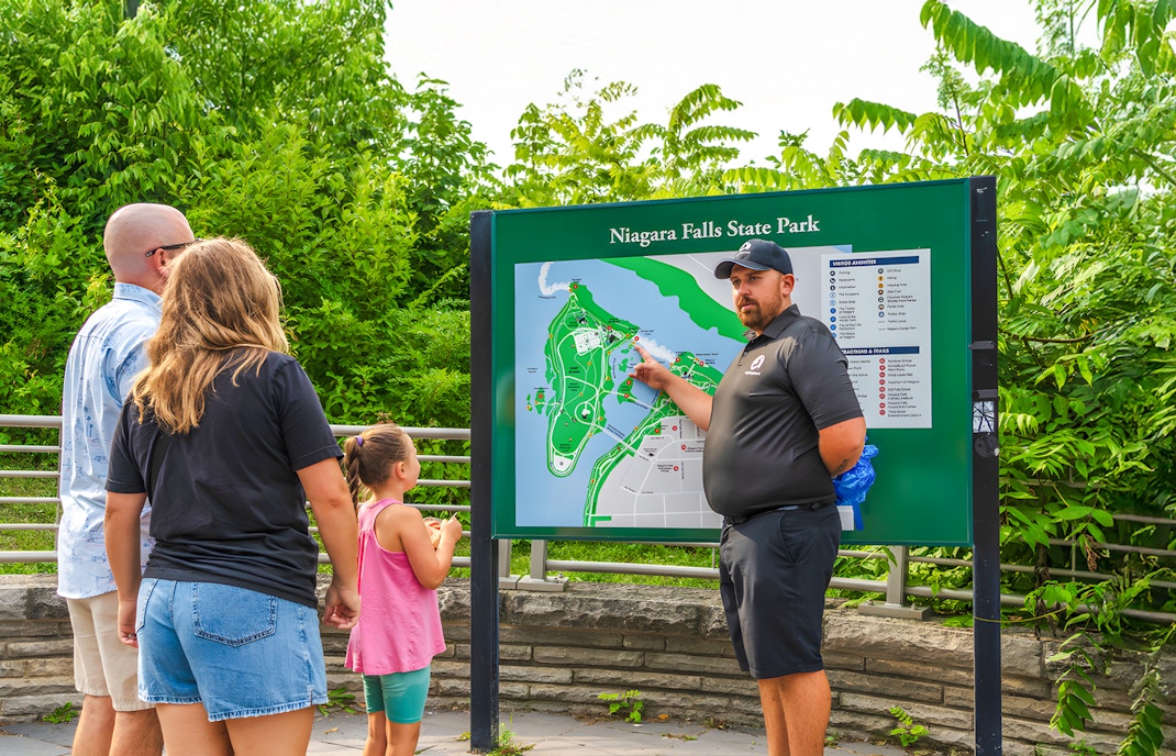 Family learning about Niagara Falls at a park map with a guide.