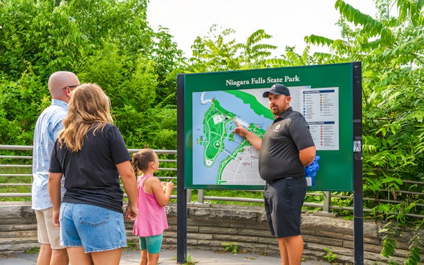 Family learning about Niagara Falls at a park map with a guide.