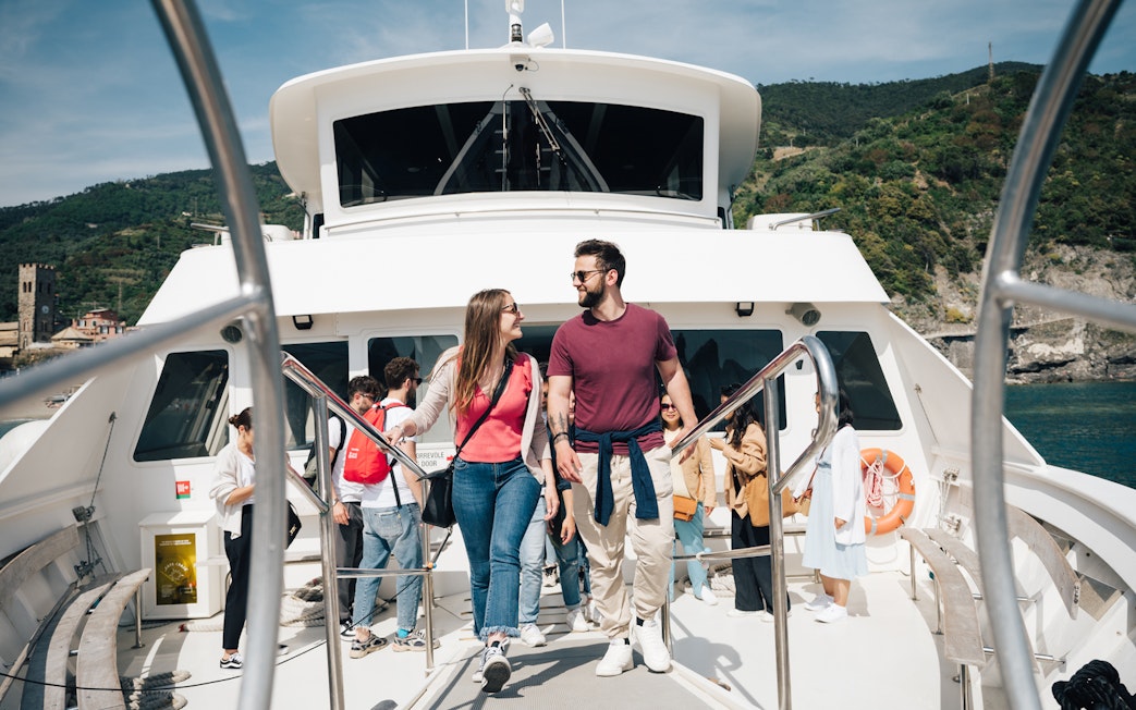 Couple walking on a boat deck with Cinque Terre coastline in the background.