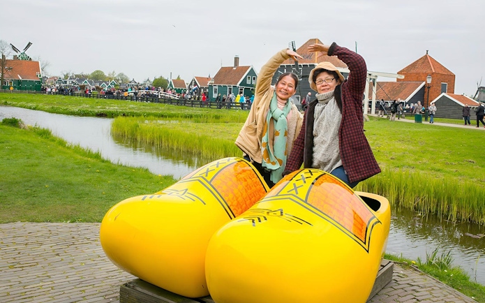 Visitors posing with giant clogs at Zaanse Schans Windmill Village near Amsterdam.