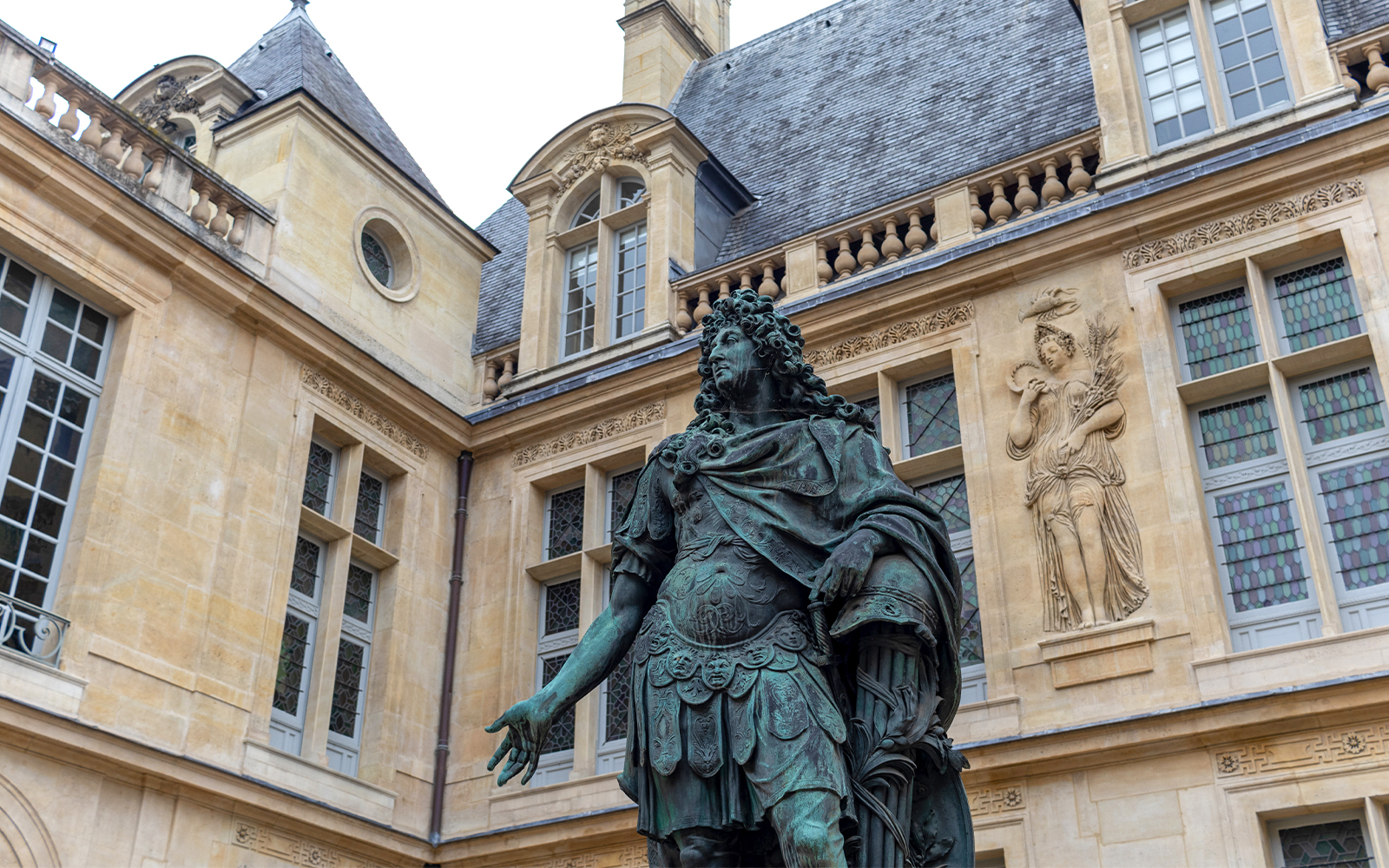 Sculpture of Louis XIV at Musée Carnavalet, Paris, with ornate building facade.