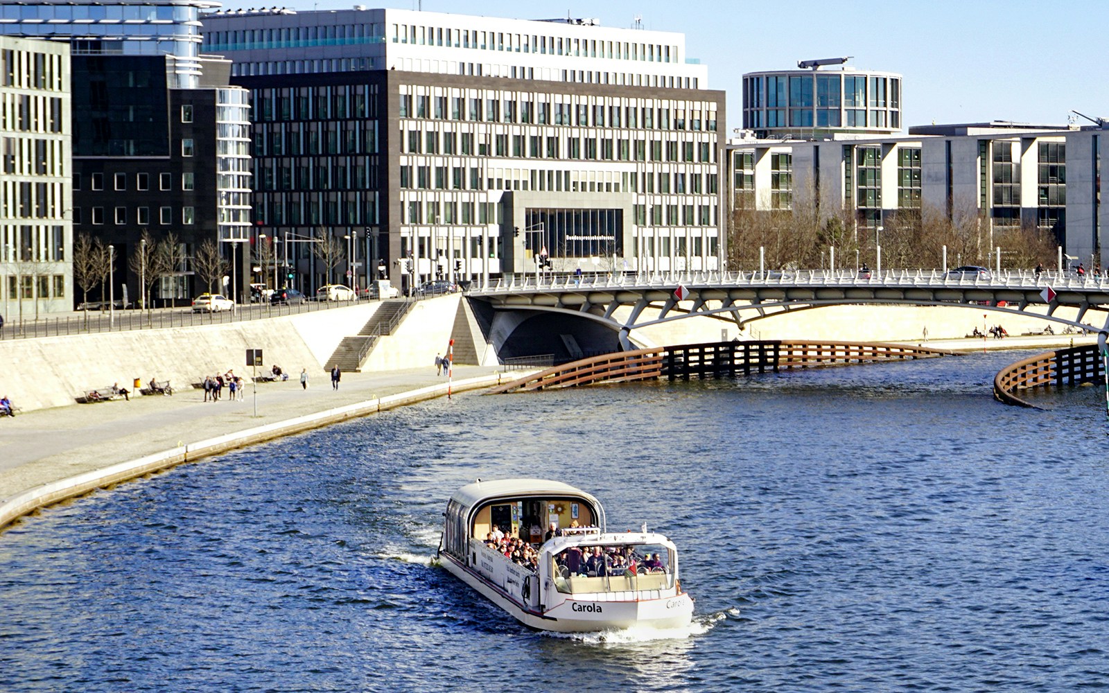 River cruise boat with tour guide on urban waterway near modern buildings.