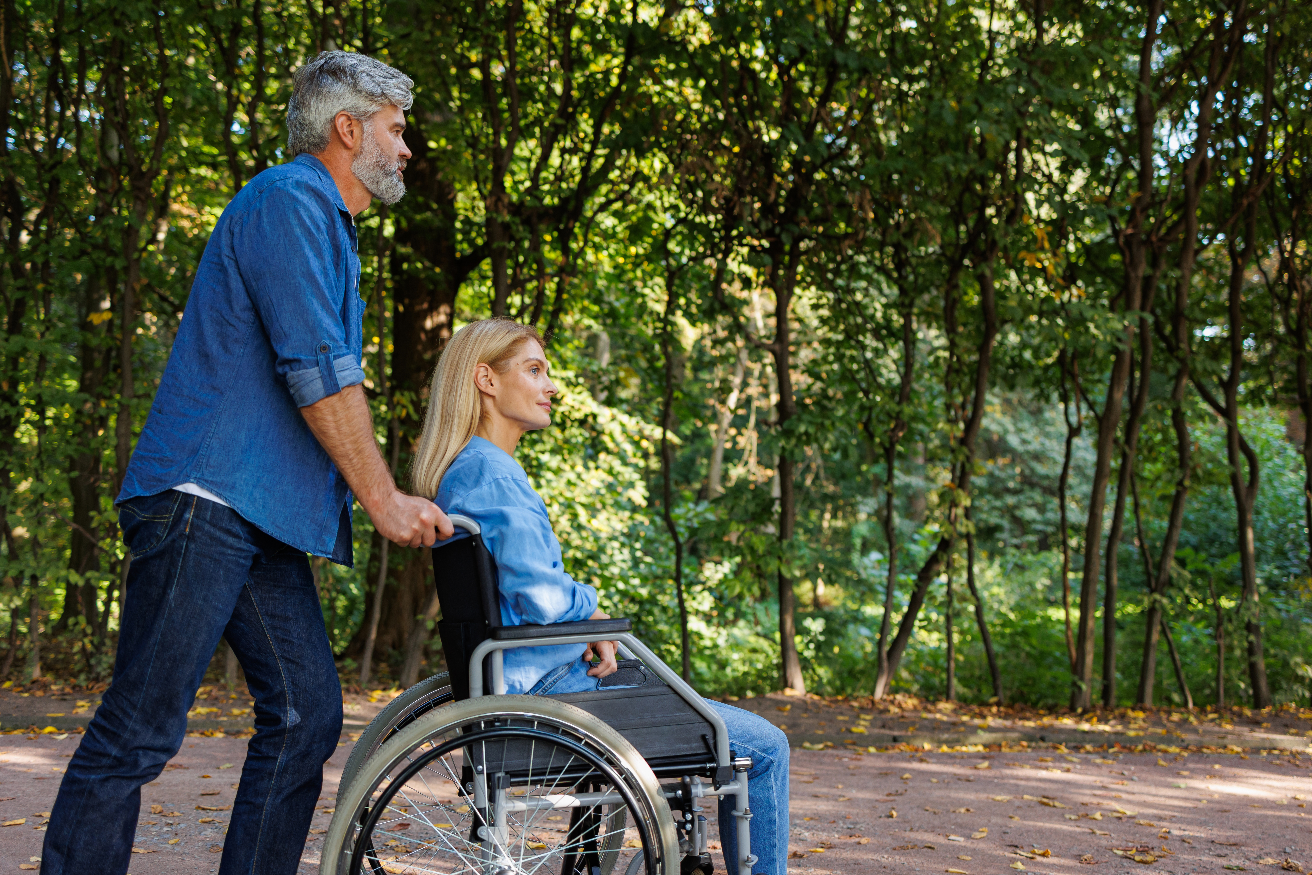 Man pushing woman in wheelchair along tree-lined path at Jardin Secret.
