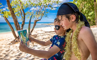 Boys dressed as pirates studying map on Frankland Islands beach.