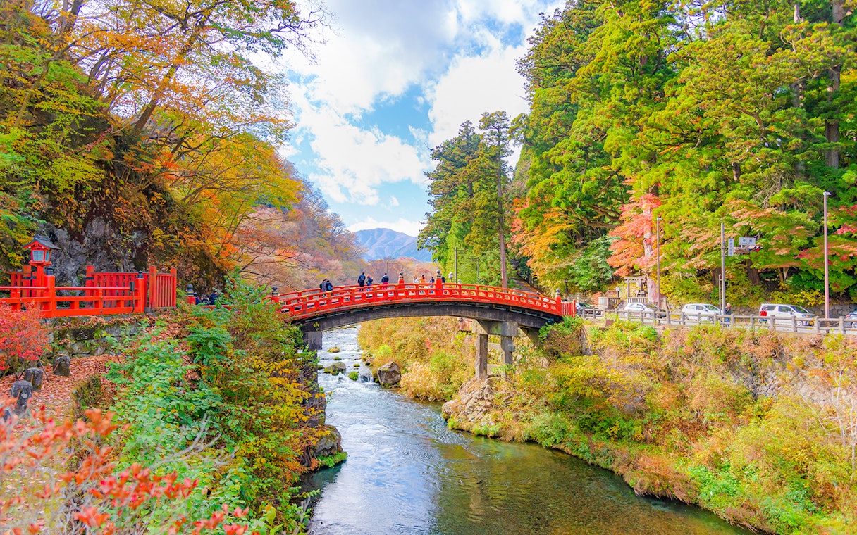 Shinkyo Bridge in Nikko, Japan, surrounded by autumn foliage and a flowing river.