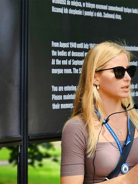 Guide explaining Auschwitz Birkenau history during a tour, standing near informational boards.